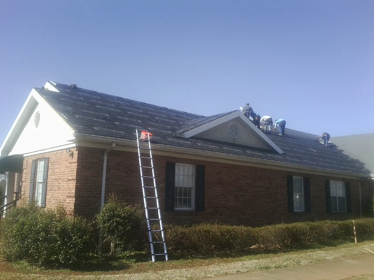 Crew tearing shingles off a brick ranch roof with a ladder set — Emergency Roof Repair work by our crew in Norwell
