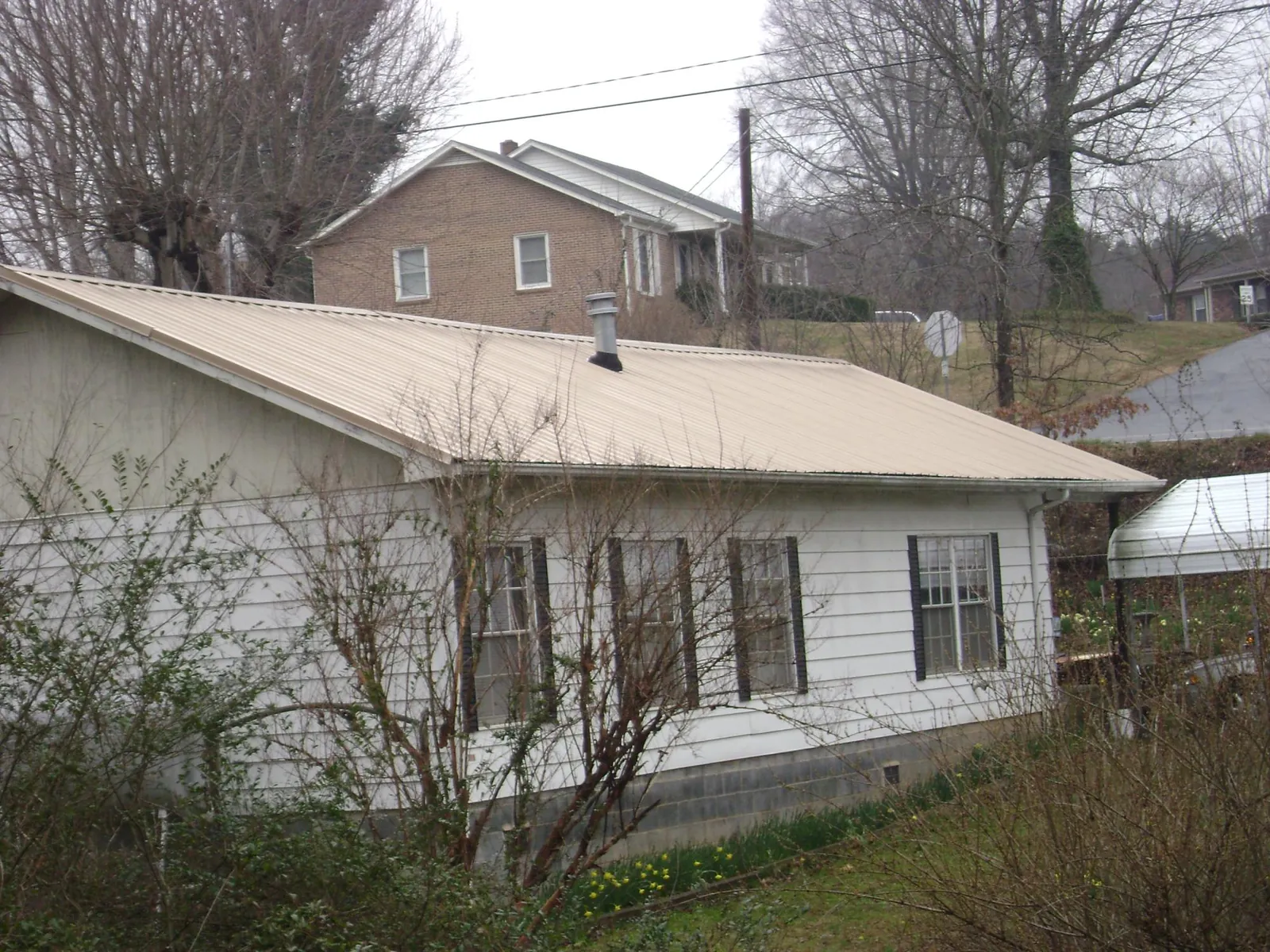 Tan metal roof on a white sided house set into a hillside — Commercial Roofing by Roofing Brothers in Norwell